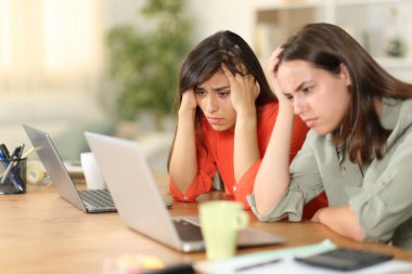 Worried tele workers checking bad news on computer at home clipart