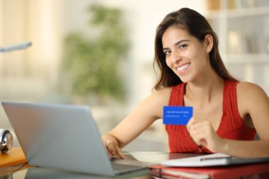 Happy student looks at you buying online with laptop and credit card clipart
