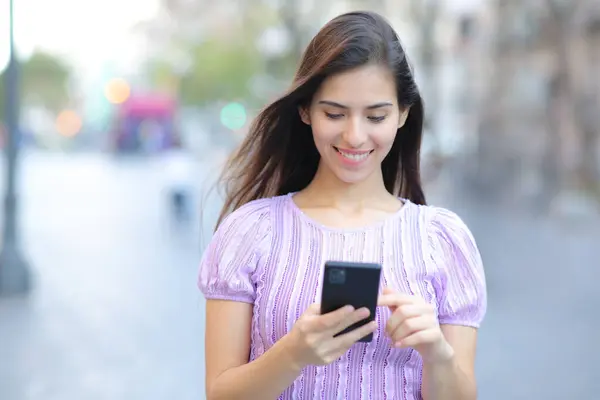 一个快乐的女人在街上用手机走路的正面肖像 免版税图库图片