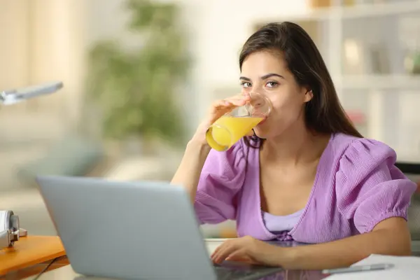 学生在网上学习喝橙汁和在家里看相机 图库照片