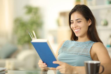 Mutlu kadın evdeki oturma odasında oturmuş kağıt kitap okuyor.