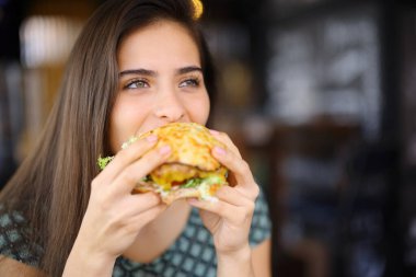 Restoranda hamburger yiyen mutlu bir kadın başka yere bakıyor.