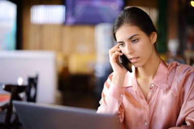 Diz üstü bilgisayarı kontrol eden zarif bir kadın barda oturmuş telefonla konuşuyor.