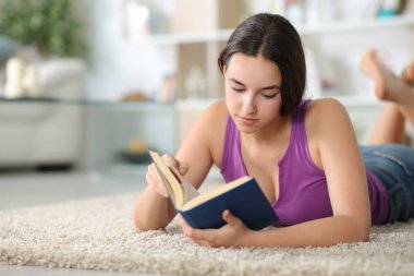 Evde yerde kitap okuyan rahat bir kadın.