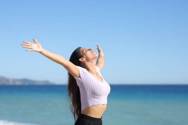 Kollarını açıp kumsalda temiz hava soluyan bir kadın.