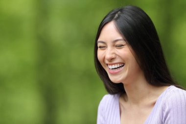 Mutlu Asyalı kadın yeşil arka planda parkta gülüyor.