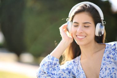 Kulaklık takan mutlu bir kadın parkta müzik dinlemekten zevk alıyor.