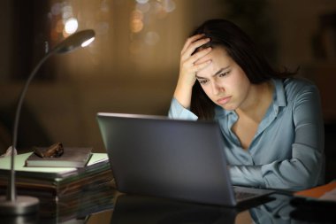 Hüsrana uğramış iş kadını gece evde dizüstü bilgisayarla çalışıyor.