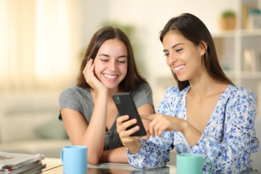 Mutlu arkadaşlar evde gülümseyen telefonları izliyorlar.