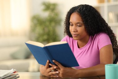 Evinde oturmuş kitap okuyan ciddi bir siyahi kadın.