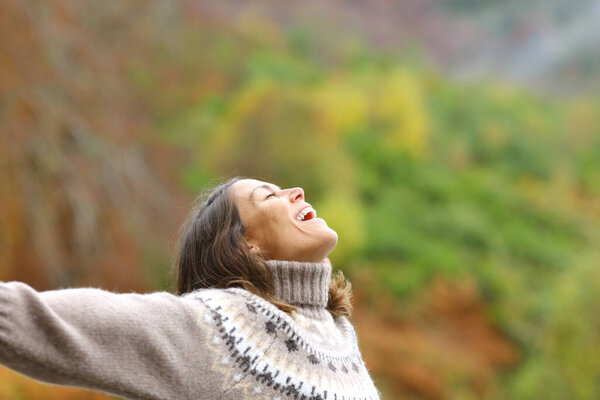Happy middle aged woman outstretching arms outdoors in nature in autumn