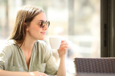 Barın içinde, güneş gözlüklü bir kadın kahve içiyor.