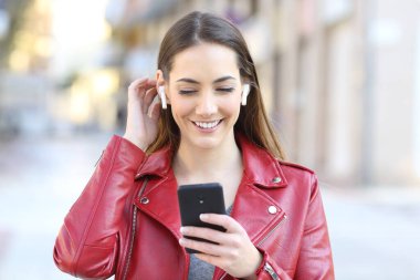 Sokakta müzik dinlemek için kulaklık ve telefon kullanan mutlu bir kadının portresi.