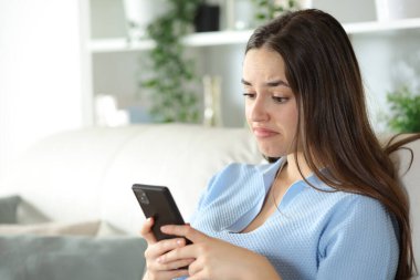 Hayal kırıklığına uğramış kadın evdeki koltukta oturan akıllı telefonu kontrol ediyor.