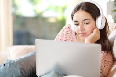 Evde dizüstü bilgisayardan kulaklık takıp film izleyen rahat bir kadın.