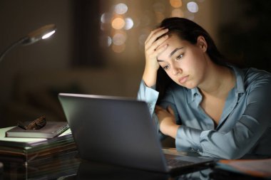 Worried tele worker checking laptop in the night at home clipart