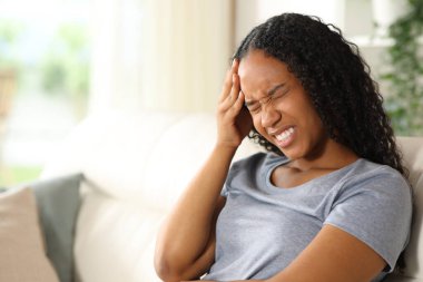 Evdeki kanepede oturan siyah kadın baş ağrısı çekiyor.