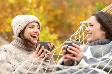 Sonbahar ormanlarında hamakta içen ve konuşan mutlu kadınlar.