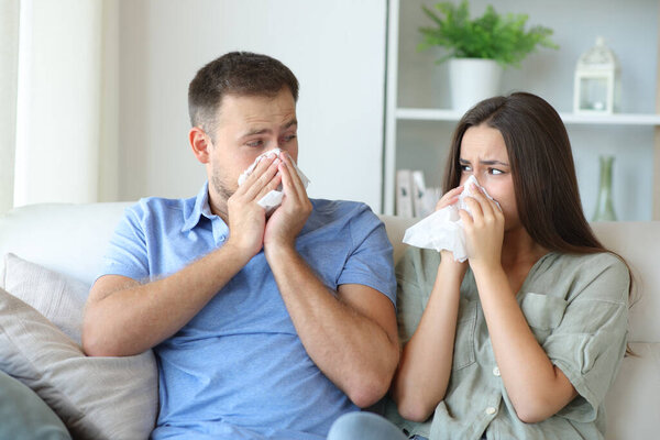 Sick couple at home blowing on tissue looking each other siting on a couch