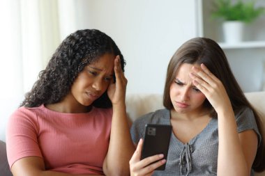 İki endişeli ırklar arası ev arkadaşı evde akıllı telefondan kötü haberleri kontrol ediyor.