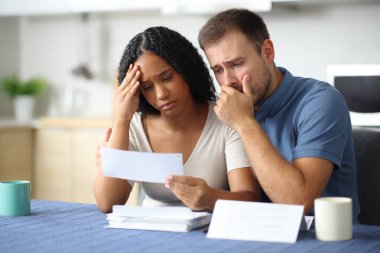 Farklı ırklardan endişeli bir çift evdeki mutfakta kitap okuyup şikayet ediyor.