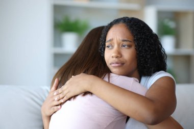 Worried black woman hugging her friend at home clipart