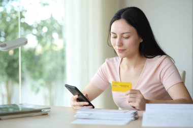 Asyalı bir kadın internet üzerinden kredi kartı ve akıllı telefonuyla faturaları ödüyor.