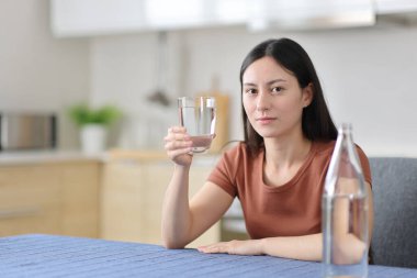 Evdeki mutfakta elinde şişe su tutan Asyalı kadın.