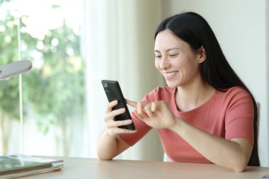Mutlu Asyalı kadın evdeki masaüstünde akıllı telefon kullanıyor.