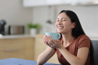 Mutlu Asyalı kadın evdeki mutfakta sıcak içecek kokusu alıyor.