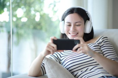 Asyalı kadın evdeki kanepede oturup video izlemek için telefon kullanıyor.