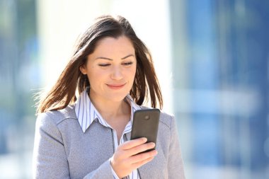 Neşeli bir yönetici, güneşli bir günde sokakta yürürken cep telefonu kullanıyor.