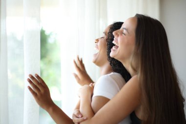 Lezbiyen, ırklar arası bir çift birlikte gülüyor. Evdeki pencerenin perdelerini açıyor.