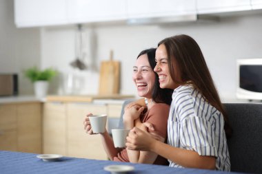 Evde çay ya da kahve içen komik lezbiyen çift mutfakta gülüyor.