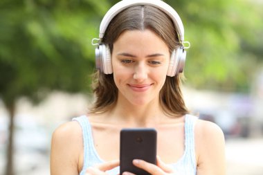 Parkta telefon kullanarak kulaklık takan tatmin olmuş bir kadının portresi.