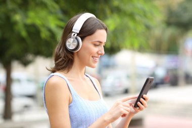 Parkta yürürken telefon ve kulaklık kullanan mutlu bir kadın.