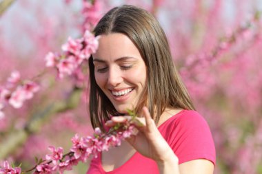 Baharda pembe bir tarlada çiçeklere dokunan mutlu dürüst kadın.