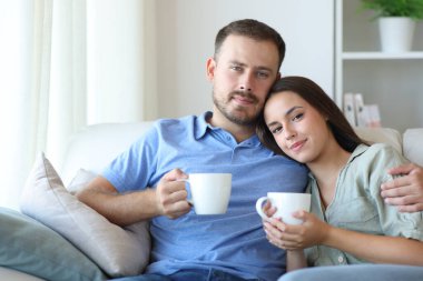 Rahat bir çift kanepede oturuyor ve kahve içiyor. Evde seni izliyorlar.