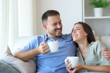 Mutlu çift evdeki kanepede oturup kahve içmekten zevk alıyor.