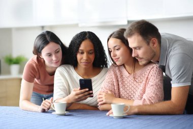 Ciddi bir ırklar arası arkadaş grubu evdeki mutfakta cep telefonunu kontrol ediyor.