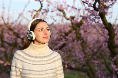 Kışın kulaklık takan bir kadın tarlada müzik dinliyor.