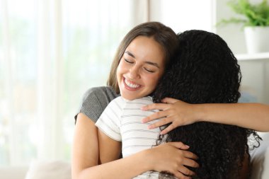 Mutlu arkadaşlar evdeki kanepede oturup sarılıyorlar. 