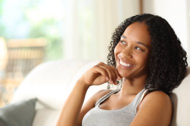 Mutlu siyahi kadın bir evde bir koltukta oturup yan gözle bakmayı düşünüyor.