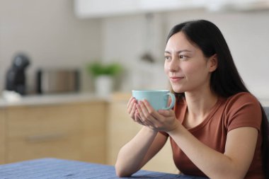 Asyalı bir kadın elinde kahve fincanıyla eve bakıyor.