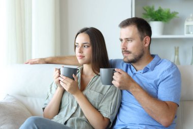 Rahatlamış bir çift çay içiyor ve evdeki bir kanepede oturuyor.