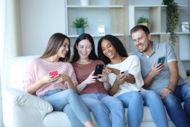 Mutlu ırklar arası arkadaş grubu evdeki koltukta oturan telefonları kontrol ediyor.
