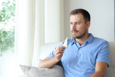 Peynir yiyen bir adam evdeki kanepede oturuyor.