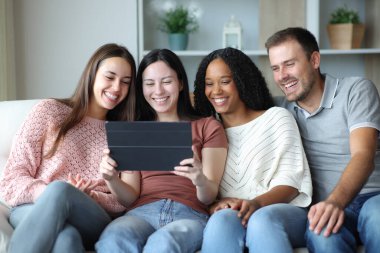 Evdeki kanepede oturup tablet kullanan mutlu ırklar arası arkadaş grubu.