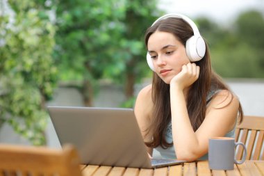 Kulaklıklı, dizüstü bilgisayar kullanan ciddi bir kadın terasta oturuyor.