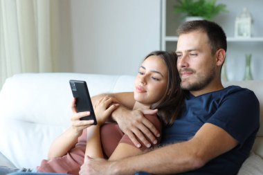 Rahat çift evdeki koltukta oturan cep telefonu içeriğini kontrol ediyor.